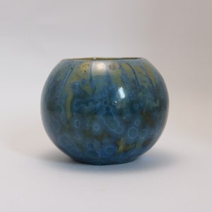 May include: A small, round ceramic vase with a blue and gold glaze. The vase has a mottled, marbled effect.