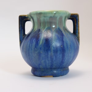 May include: A ceramic vase with two handles, featuring a rounded body and a flared base. The vase is glazed in shades of blue and green, with a glossy finish. The handles are a darker brown color.