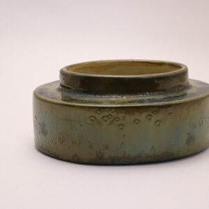 May include: A green and brown ceramic bowl with a speckled glaze. The bowl has a rounded shape and a slightly raised rim.