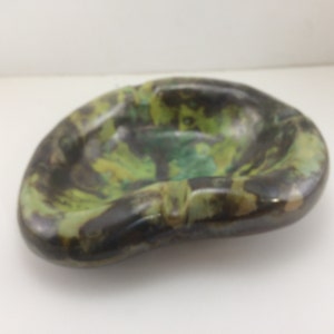 May include: A green, brown, and black ceramic ashtray with a unique, abstract design. The ashtray is shaped like a leaf and has a smooth, glossy finish.