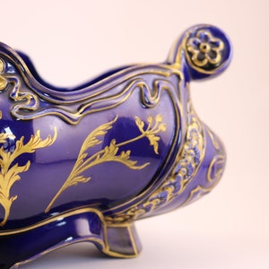 Puede incluir: Un cuenco de cer&aacute;mica azul cobalto con dise&ntilde;os florales dorados. El cuenco tiene un borde festoneado y un asa decorativa.