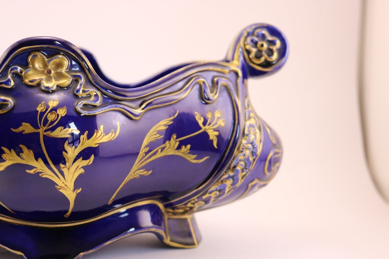 Puede incluir: Un cuenco de cer&aacute;mica azul cobalto con dise&ntilde;os florales dorados. El cuenco tiene un borde festoneado y un asa decorativa.