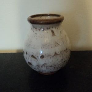 May include: A small, white ceramic vase with a brown rim. The vase has a textured surface with brown speckles.