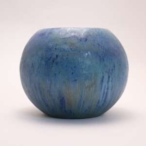 May include: A round, blue ceramic vase with a mottled glaze. The vase has a smooth, rounded shape and a light blue color with streaks of darker blue and white.