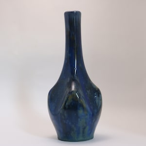 May include: A blue ceramic vase with a unique, abstract shape. The vase has a narrow neck and a wide, rounded base.