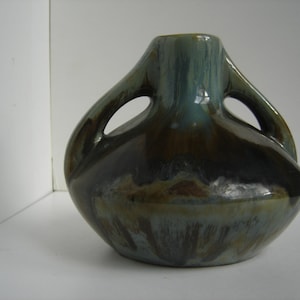 May include: A small, brown and blue ceramic vase with two handles. The vase has a unique, abstract design.