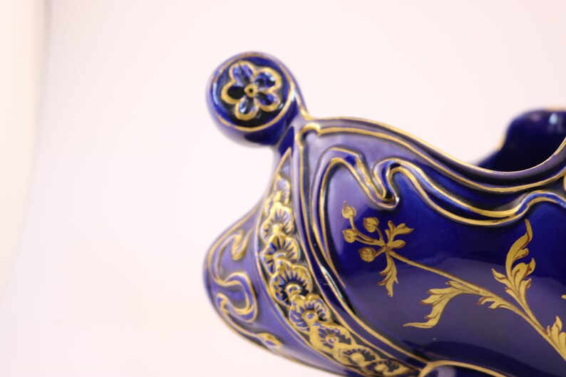 Puede incluir: Un cuenco de cer&aacute;mica azul y dorado con un dise&ntilde;o floral. El cuenco tiene un borde festoneado y un asa decorativa.