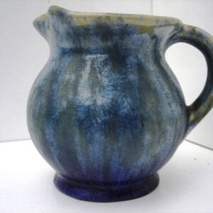 May include: A small blue and green ceramic pitcher with a textured glaze. The pitcher has a rounded body and a handle.