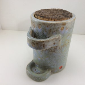 May include: A ceramic jar with a cork lid and a handle. The jar has a speckled blue and brown glaze with a light brown base. The jar has a small spout on the side.