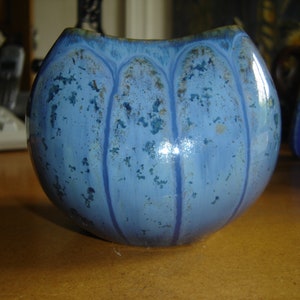 May include: A blue ceramic vase with a glossy finish and a textured surface. The vase has a rounded shape and a wide opening.