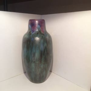 May include: A dark green ceramic vase with a purple and pink glaze at the top. The vase has a rounded body and a narrow neck.