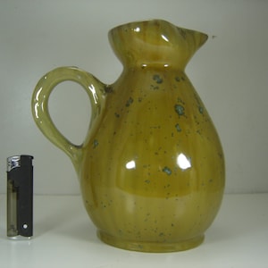May include: A yellow ceramic pitcher with a speckled glaze and a wide, rounded body. The pitcher has a handle and a spout.
