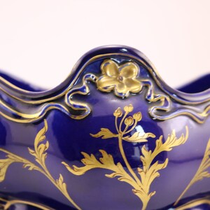 Puede incluir: Un cuenco de cer&aacute;mica azul y dorado con un dise&ntilde;o floral decorativo. El cuenco tiene un borde festoneado y una boca ancha y abierta.