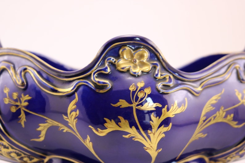 Puede incluir: Un cuenco de cer&aacute;mica azul y dorado con un dise&ntilde;o floral decorativo. El cuenco tiene un borde festoneado y una boca ancha y abierta.