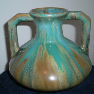 May include: A large, ceramic vase with two handles. The vase is decorated with a green and brown glaze that creates a marbled effect.