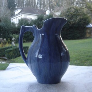 May include: A blue ceramic pitcher with a textured glaze. The pitcher has a rounded body and a curved handle.