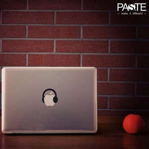 Può includere: Un computer portatile argentato con un paio di cuffie nere e un adesivo con il logo Apple sul coperchio. Il computer portatile è appoggiato su un tavolo di legno davanti a un muro di mattoni rossi. Una mela rossa è appoggiata sul tavolo a destra del computer portatile.