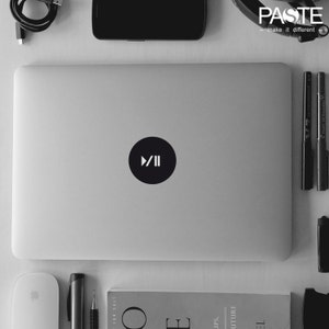 Könnte beinhalten: Ein schwarz-weißer Aufkleber mit einem Play- und Pause-Knopfsymbol auf einem silbernen Laptop.