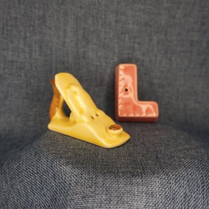 May include: A yellow ceramic hand plane and a pink ceramic letter L. Both are salt and pepper shakers.