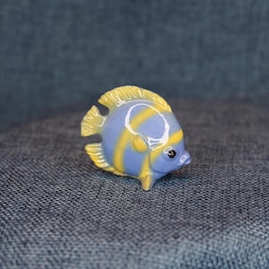 May include: A small ceramic figurine of a blue and yellow angelfish. The fish has a white stripe around its eye and yellow stripes on its body.