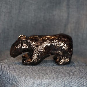 May include: A small, glossy black figurine shaped like a bear in a walking stance. The surface of the bear is highly reflective, showing bright highlights across its rounded back, head, and legs, creating a smooth, polished appearance.
