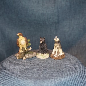 May include: Three miniature animal figurines: a hawk perched on a branch, a black bear, and a howling wolf. The hawk has brown and tan feathers. The bear is black. The wolf is gray and white. All are on small bases.