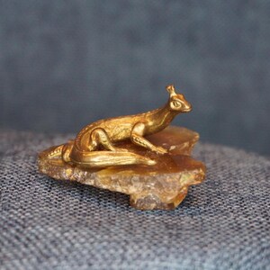 May include: A gold-colored lizard figurine perched on a piece of amber.