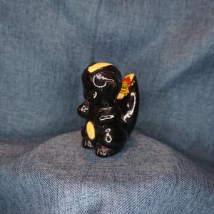 May include: A black and white ceramic figurine of a skunk. The skunk is standing on its hind legs with its tail curled up. The figurine has a glossy finish.