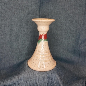 May include: A white ceramic candle holder with a speckled glaze and a red and green band around the middle.