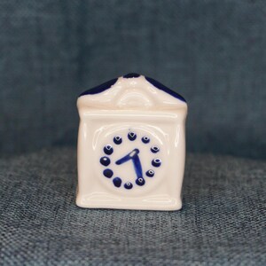May include: A white ceramic clock with a blue and white design. The clock face has a blue number one and blue dots around the edge.