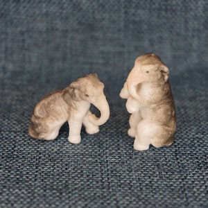May include: Two small ceramic elephant figurines. One is gray and white, the other is white with gray accents.
