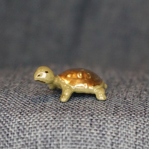 May include: A small, ceramic turtle figurine with a green body and a gold shell. The turtle is sitting on a blue denim fabric.