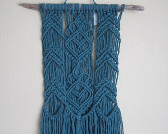 May include: Teal blue macrame wall hanging with a wood dowel and fringe.