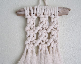 May include: A white macrame wall hanging with a driftwood top and fringe tassels.