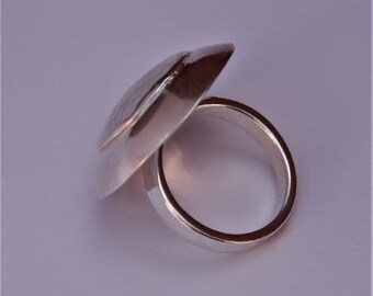 May include: A silver ring with a unique, rounded, and slightly domed top. The top of the ring is smooth and has a subtle groove running around its circumference.