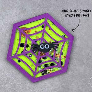 May include: A purple and green hexagon-shaped craft with a spider web design. The web is filled with glitter and googly eyes. The text "ADD SOME GOOGLY EYES FOR FUN!" is written above the craft.