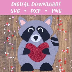 May include: A gray raccoon holding a red glitter heart. The raccoon is smiling and has a black nose and eyes. The background is a wooden surface with red and white hearts scattered around.