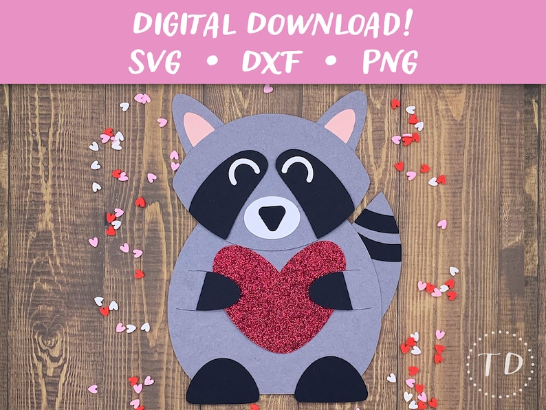 May include: A gray raccoon holding a red glitter heart. The raccoon is smiling and has a black nose and eyes. The background is a wooden surface with red and white hearts scattered around.