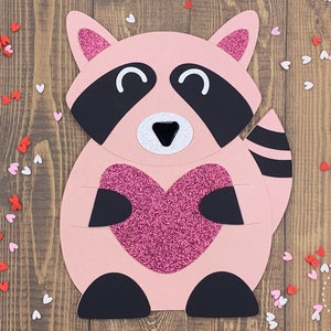 May include: A pink raccoon holding a pink glitter heart. The raccoon has black eyes, a black nose, and a black and white striped tail. The background is a wooden surface with pink and white hearts scattered around.