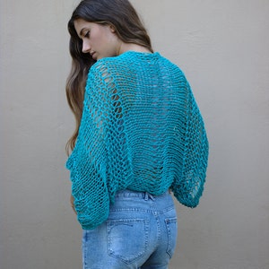 Peut inclure: Un haut en crochet turquoise avec un design lâche et à mailles ouvertes. Le haut est porté sur un short en jean.