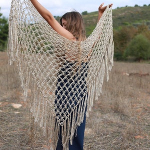 May include: A beige crochet shawl with fringe. The shawl is made of a delicate, open-weave fabric and has a flowing, ethereal look.