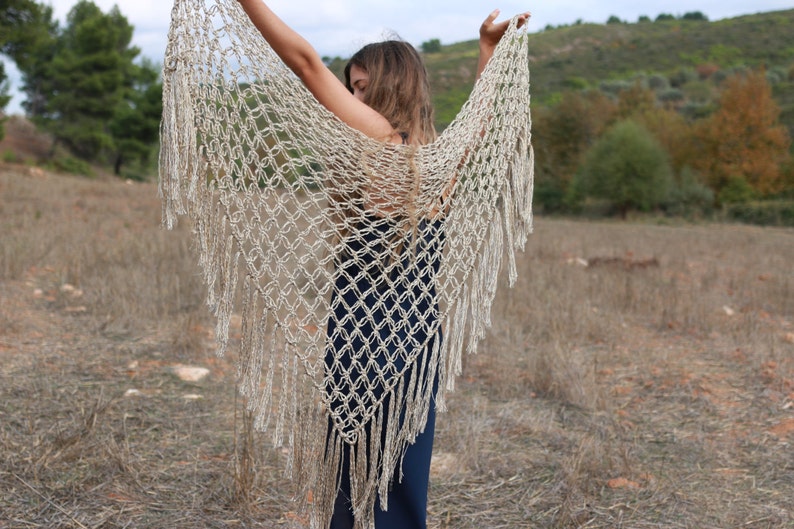 May include: A beige crochet shawl with fringe. The shawl is made of a delicate, open-weave fabric and has a flowing, ethereal look.