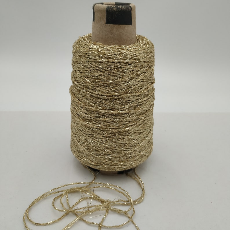 May include: A spool of gold metallic thread with a cardboard center. The thread is loose and unraveled at the bottom of the spool.