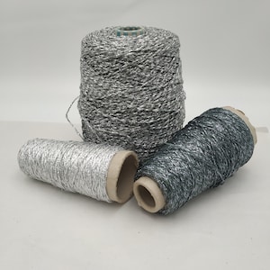 May include: Three spools of metallic yarn, one silver and two dark gray. The yarn is wound around cardboard spools.