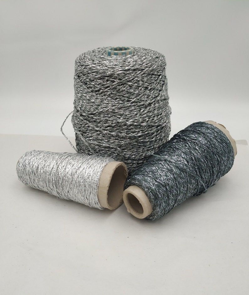 May include: Three spools of metallic yarn, one silver and two dark gray. The yarn is wound around cardboard spools.