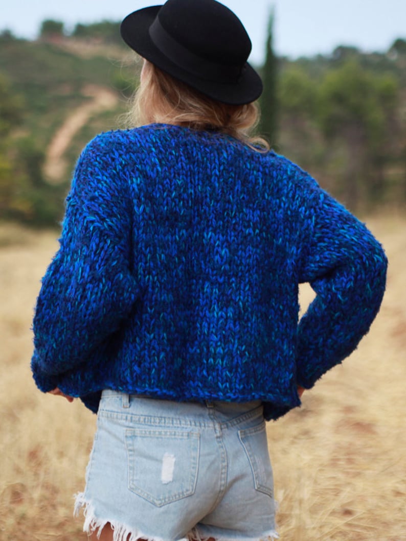 May include: A blue and green chunky knit sweater with a relaxed fit. The sweater is cropped and has a slightly oversized look.