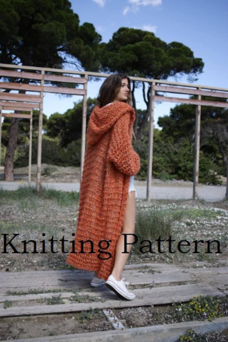 May include: A long, orange knitted cardigan with a hood. The cardigan is made with a fluffy yarn and has a relaxed fit. The model is wearing the cardigan with white trainers.