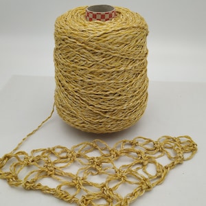 May include: A spool of gold yarn with a crocheted piece made from the yarn. The yarn has a shimmery, textured look.