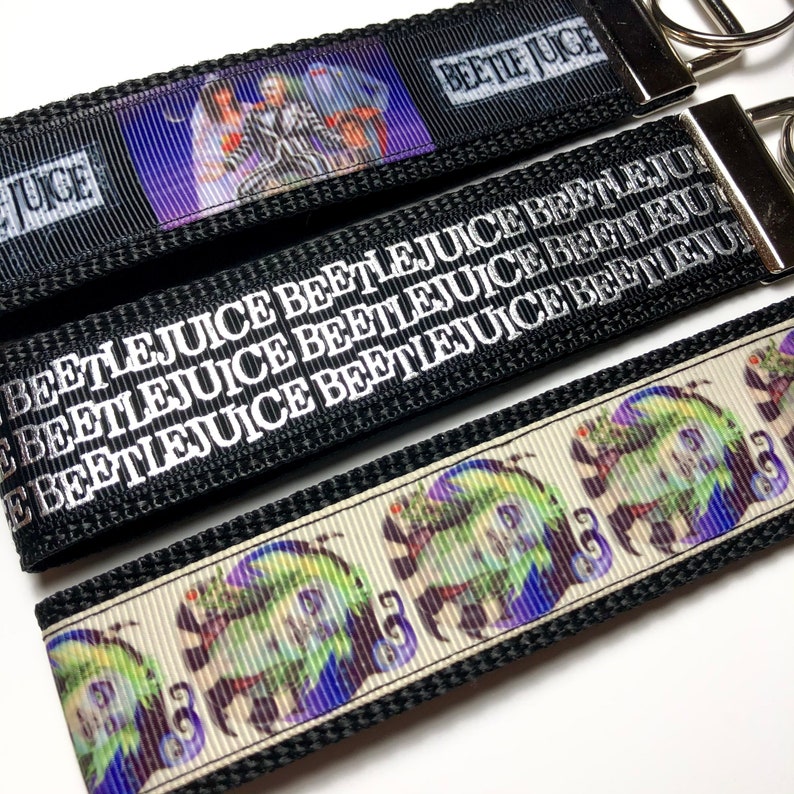 May include: Three black and white keychains with the text "Beetlejuice" repeated multiple times. One keychain features a printed image of the characters from the movie Beetlejuice.