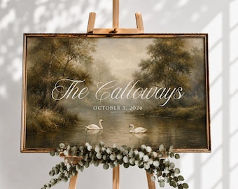 May include: A rectangular landscape painting in a dark wood frame displayed on a wooden easel. The artwork depicts a serene river scene with two white swans, lush trees, and the text The Calloways and OCTOBER 3, 2026. Green foliage decorates the base.